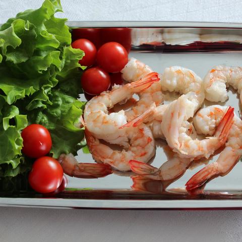 A platter of cooked shrimp with lettuce and cherry tomatoes